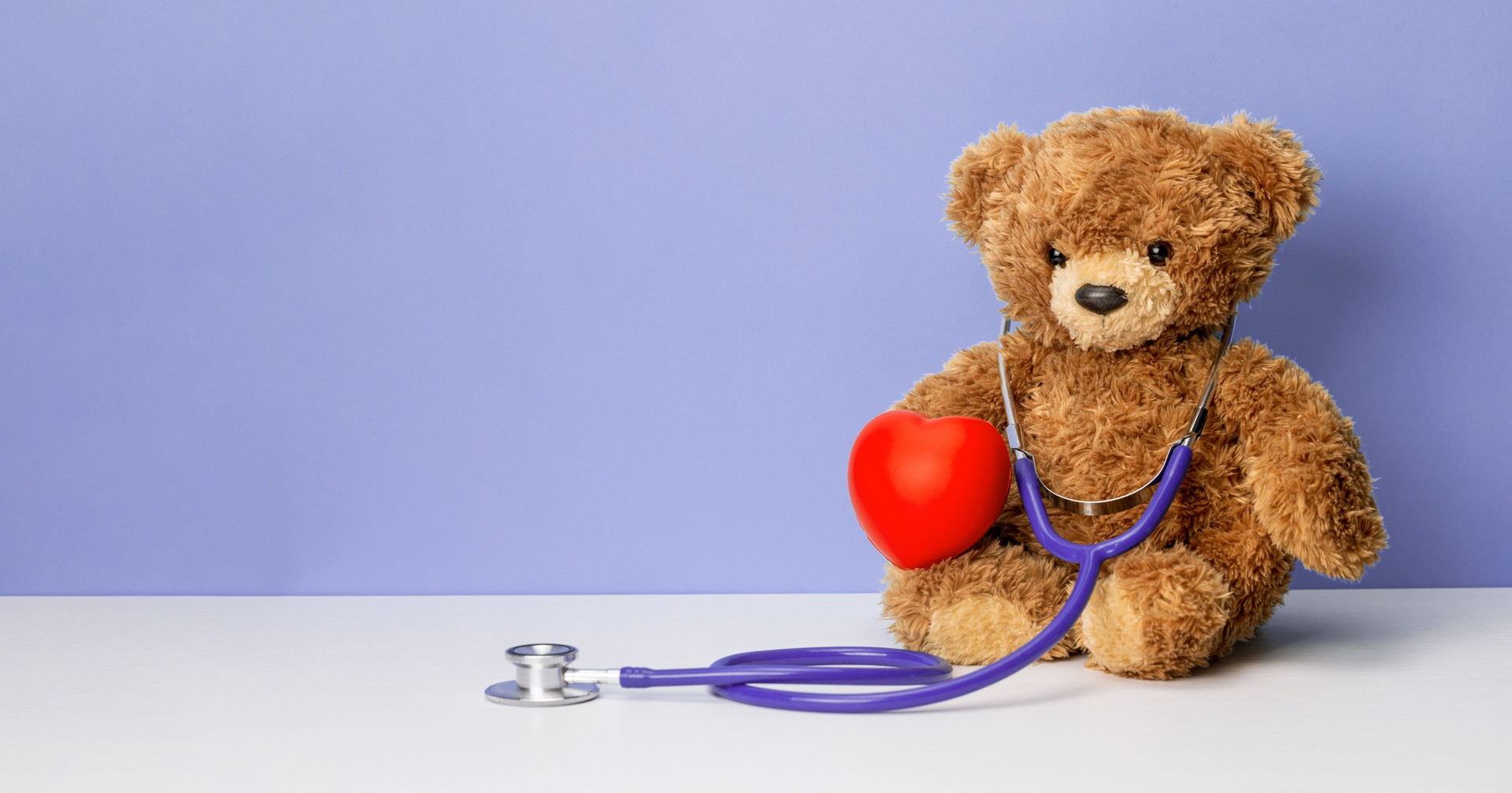 Teddy bear with a stethoscope and a heart on a purple background. Family doctor or pediatrician concept