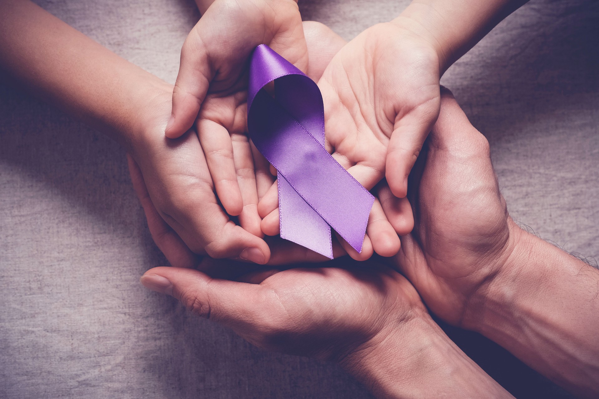 Adult and child hands holding purple ribbons, Alzheimer's disease, Pancreatic cancer, Epilepsy awareness, world cancer day